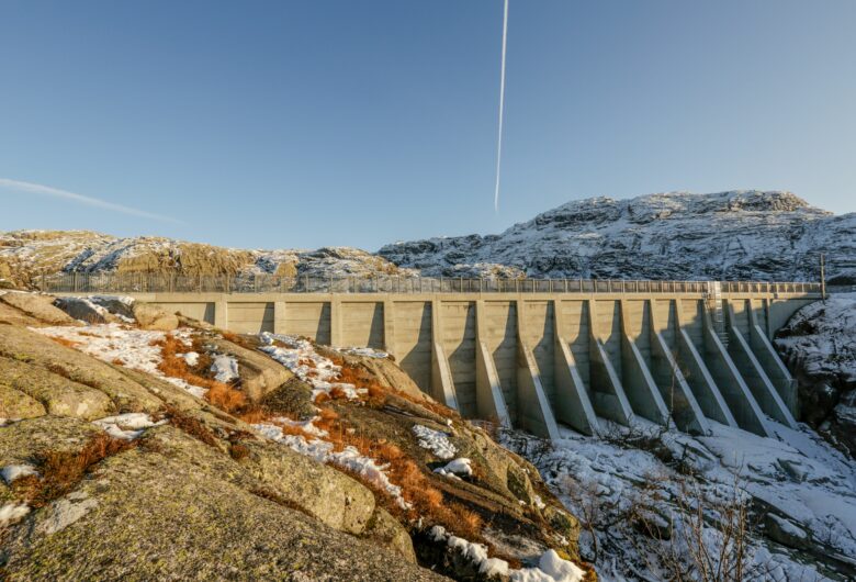 Dam Finflot etter rehabilitering. Solen går ned over betongdammen. Fjelltoppene i bakgrunnen er dekket med snø,