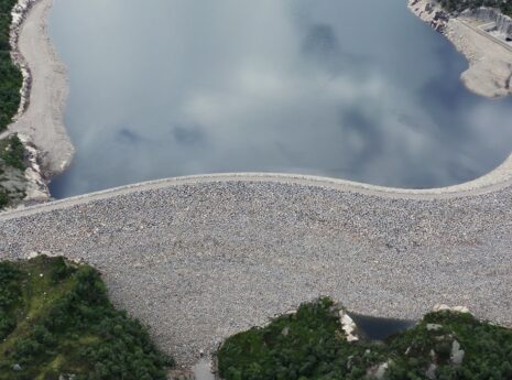 Oversiktsbilde over en nybygget dam. Grå steiner dekker den store dammen, blått hav og grønn skog rundt.